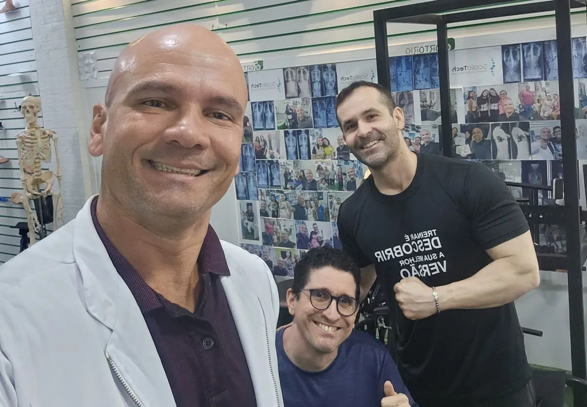 Léo em selfie sorridente com um paciente em cadeira de rodas e um treinador no centro
